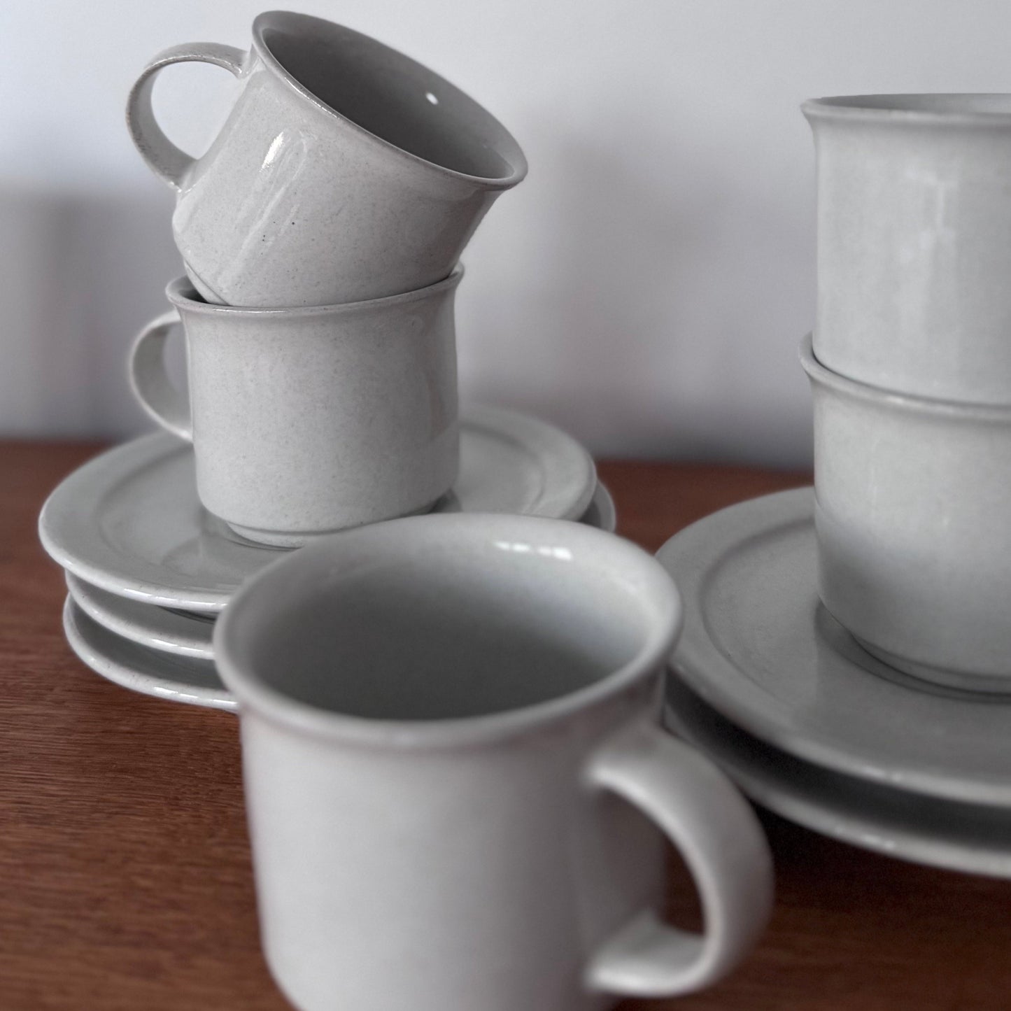 Höganäs Keramik tea set with white ceramic mugs and matching plates, neatly stacked on a wooden surface.