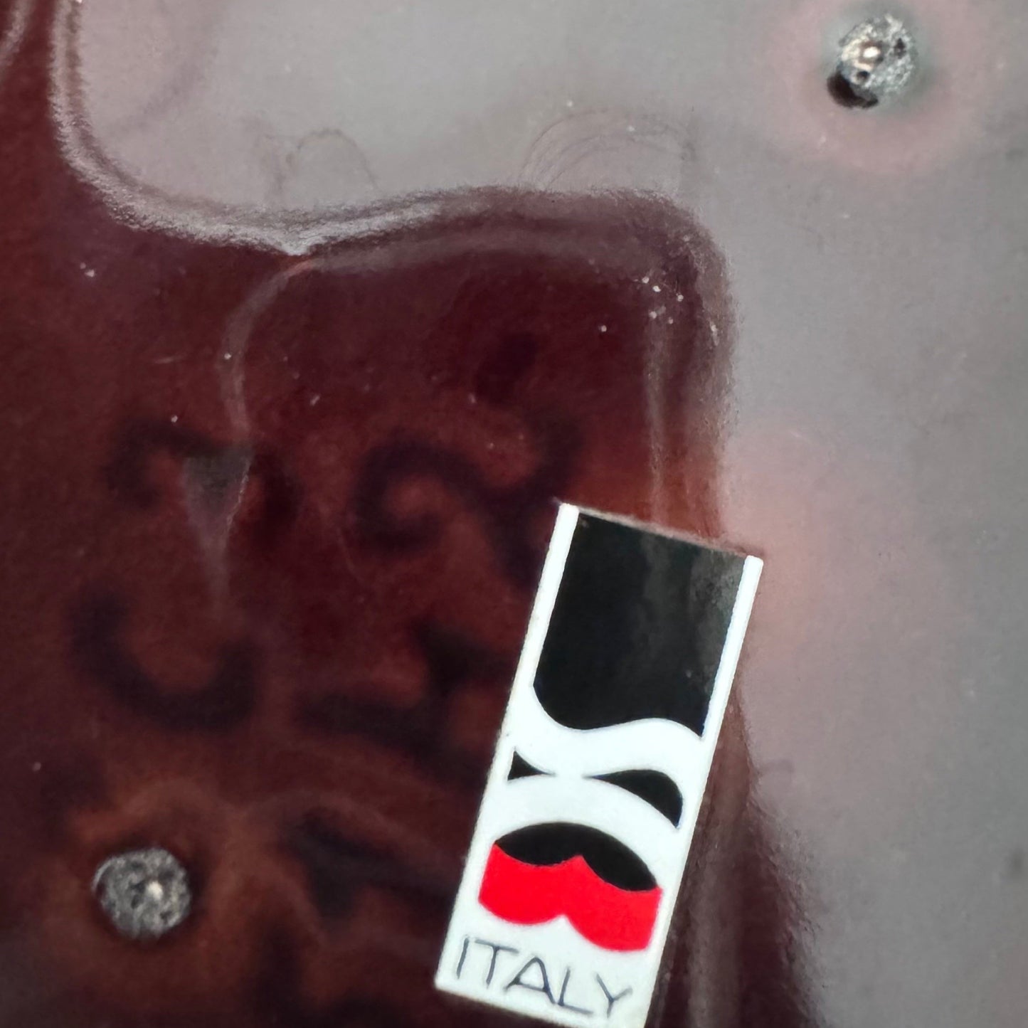 Close-up of a maker’s mark on a glossy dark brown ceramic base, showing a stylized black and red logo with the word “ITALY” underneath.