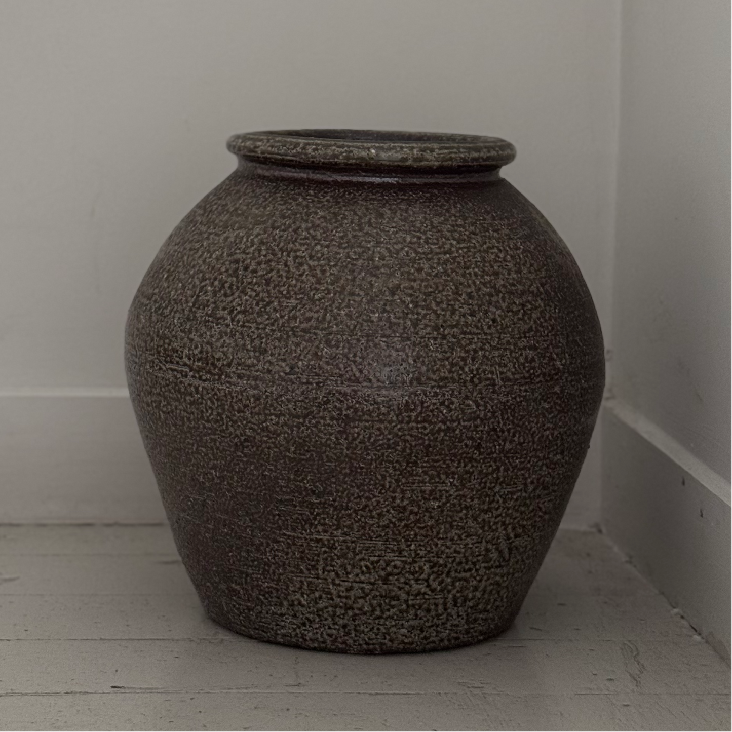 Textured vase on a light wooden floor against a white wall