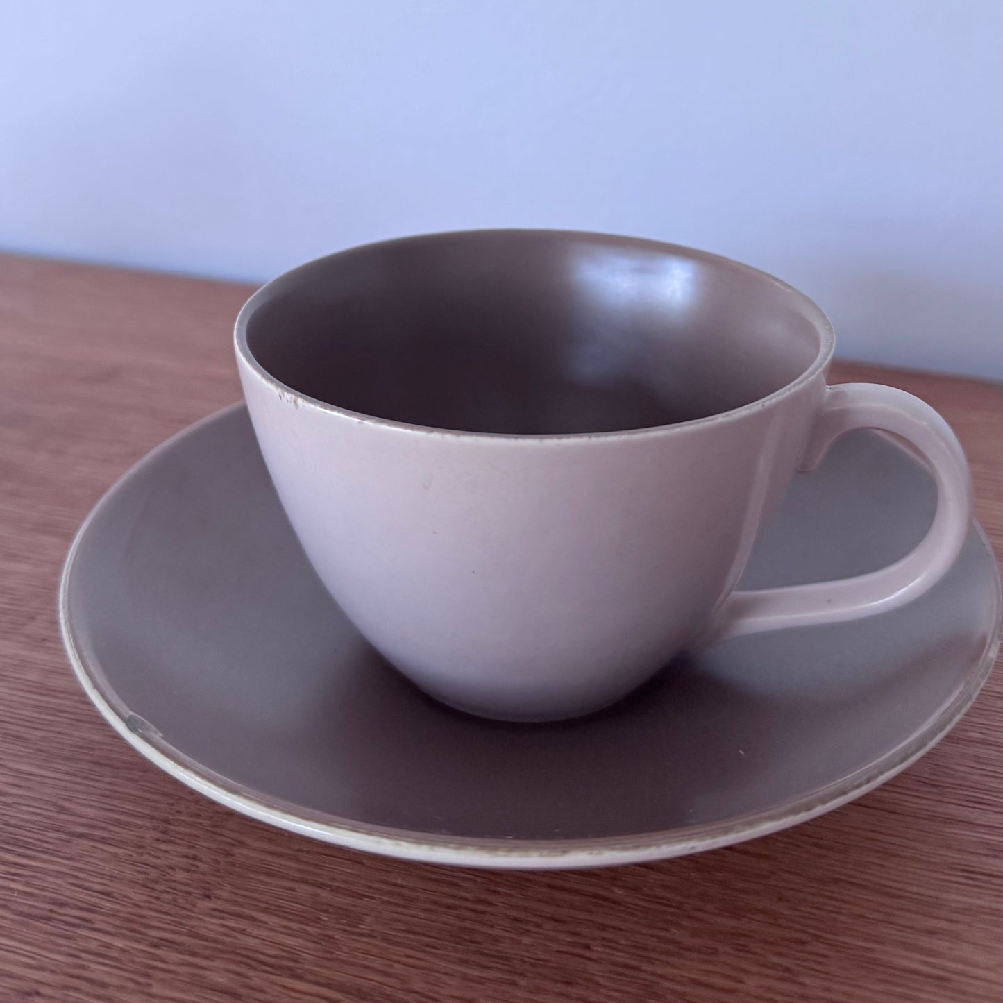 Mauve and brown Poole Pottery cups, jug, and serving dishes stacked neatly on a wooden surface
