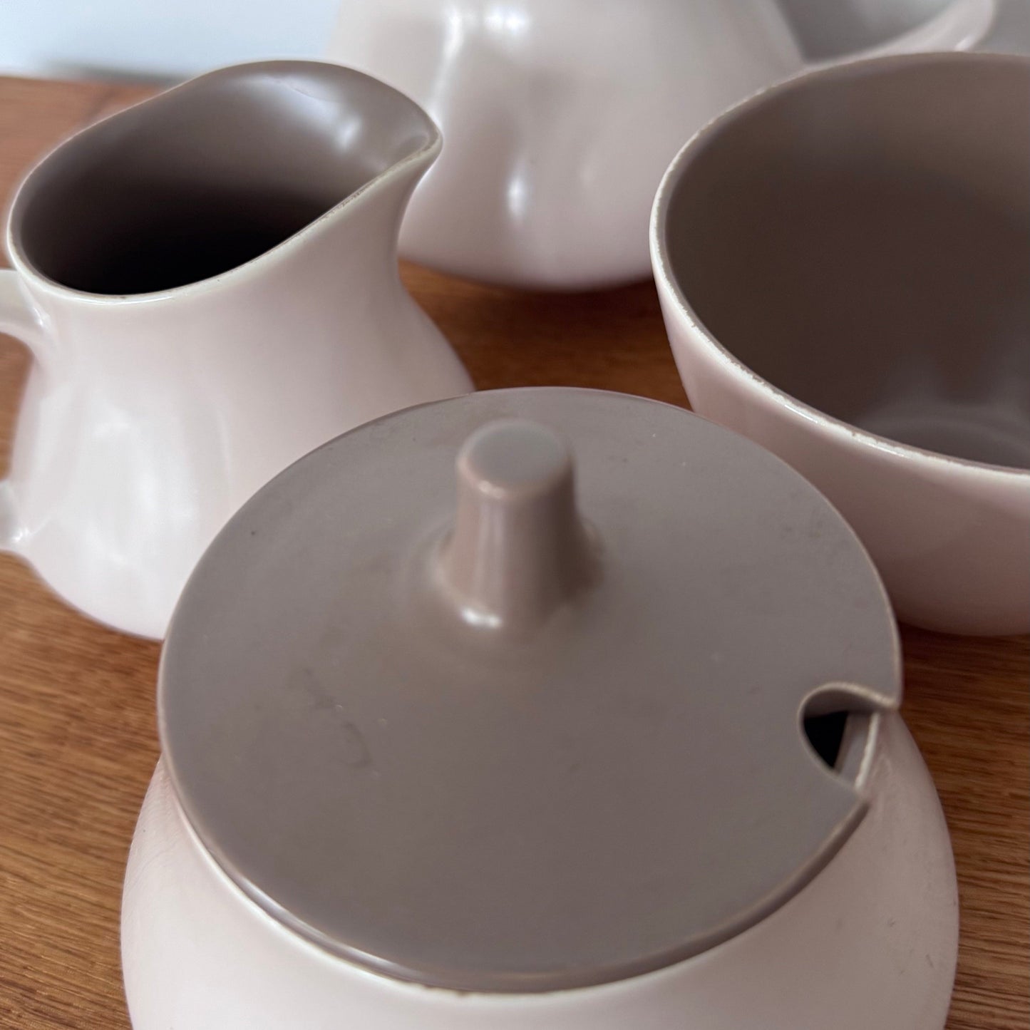 Mauve and brown Poole Pottery cups, jug, and serving dishes stacked neatly on a wooden surface