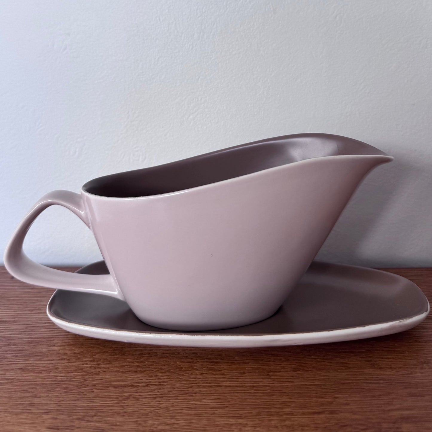 Mauve and brown Poole Pottery bowls and serving dishes stacked neatly on a wooden surface