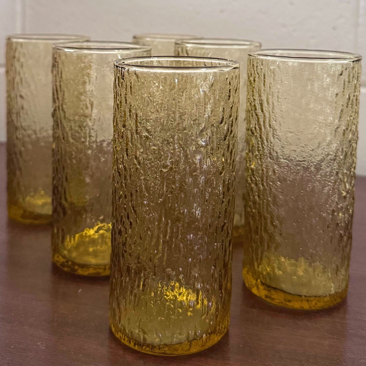 Set of six tall vintage amber drinking glasses with textured ice-like surface, standing on a wooden surface