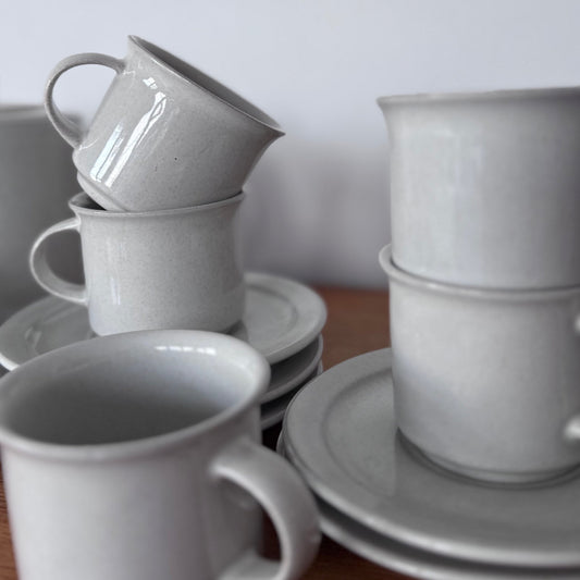 Höganäs Keramik tea set with white ceramic mugs and matching plates, neatly stacked on a wooden surface.