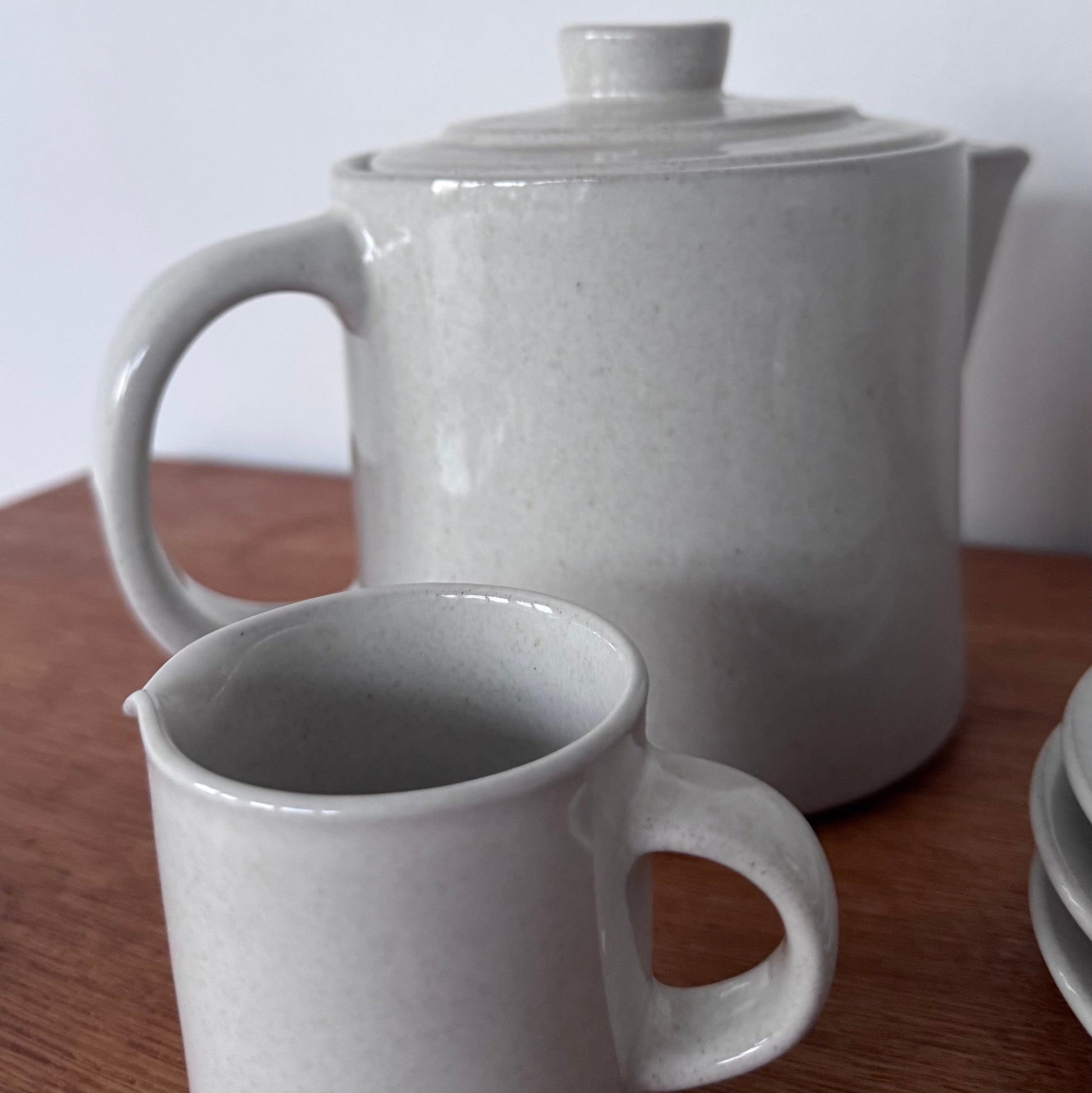 Höganäs Keramik tea set with white ceramic mugs and matching plates, neatly stacked on a wooden surface.