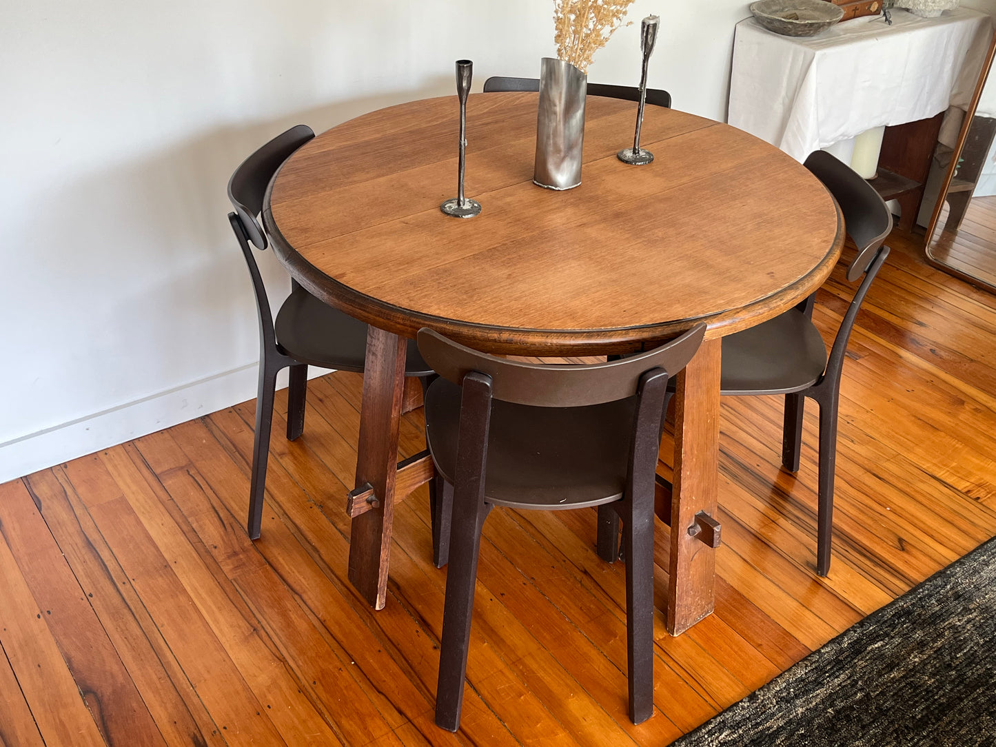 Round wooden dining table with four dark chairs on a wooden floor.