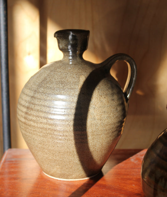Ceramic vase with textured surface and dark handle on a wooden surface