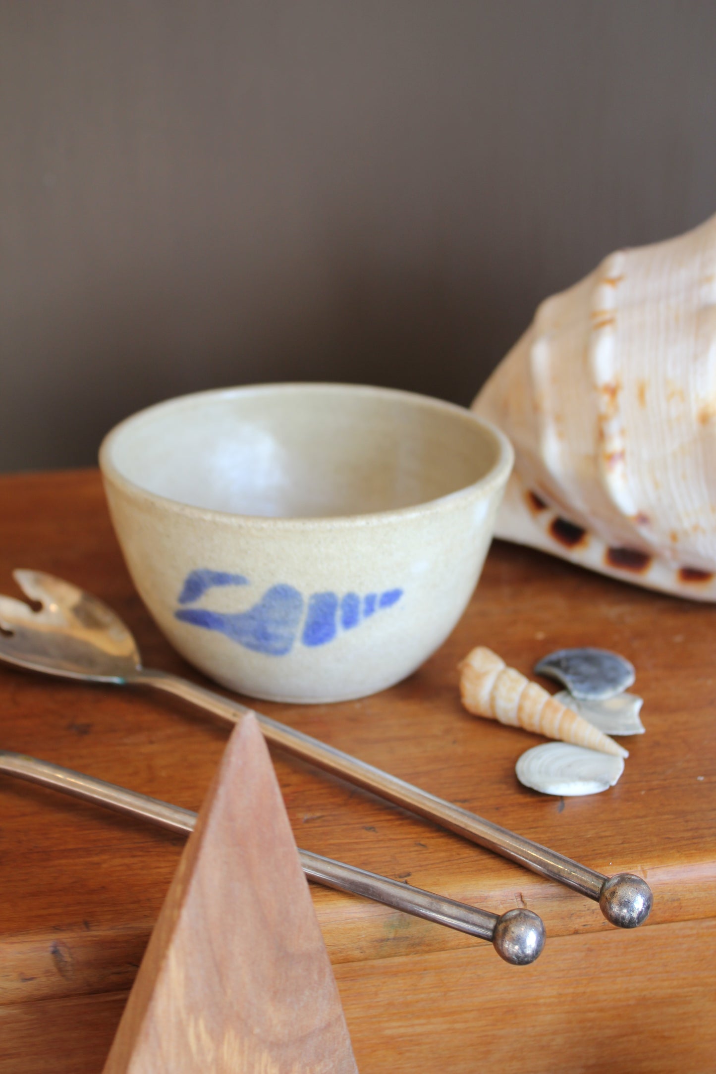 Ceramic cup with blue design on a wooden surface with shells and spoons.
