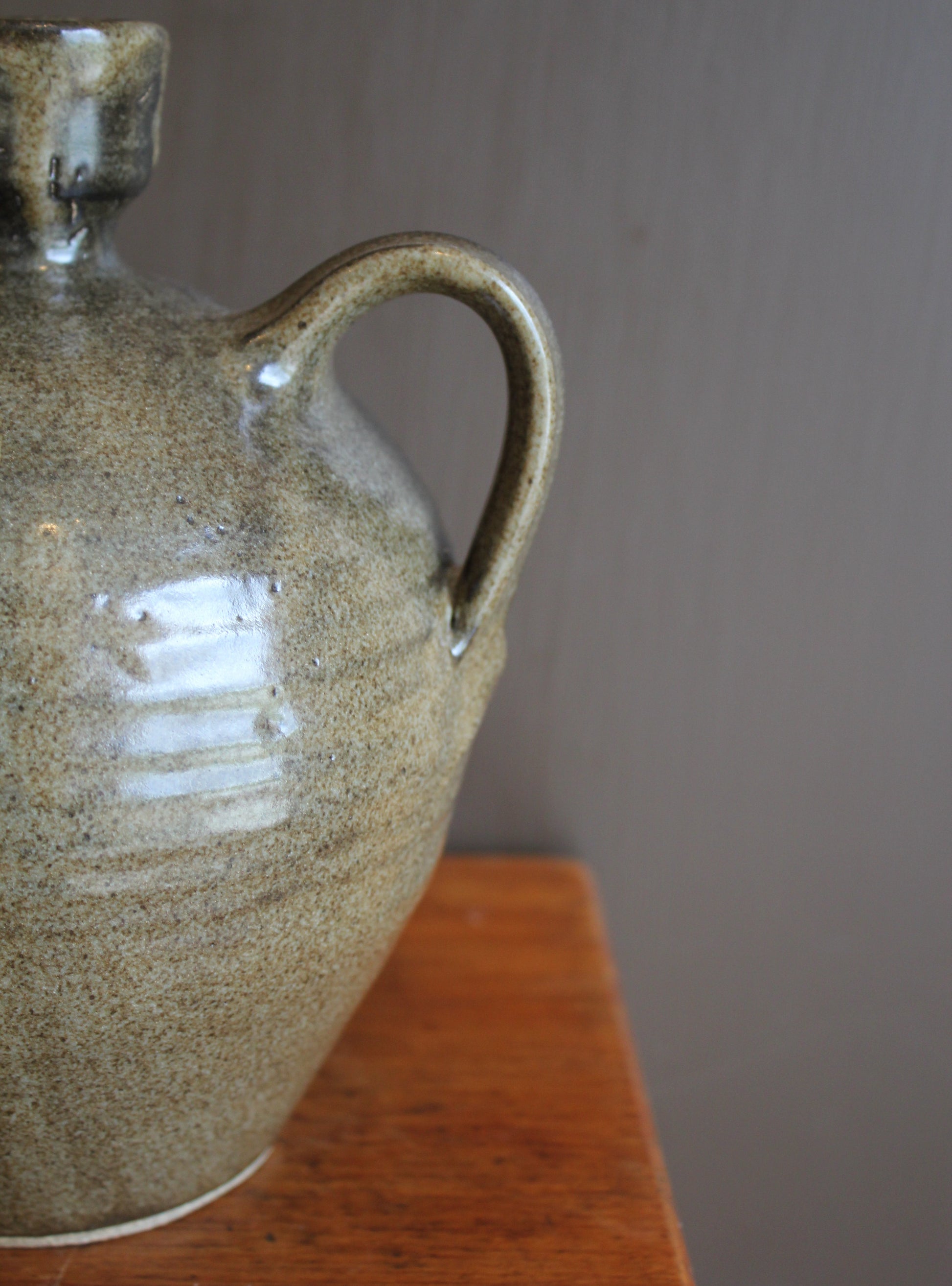 Ceramic jar with a handle on a wooden surface against a gray wall