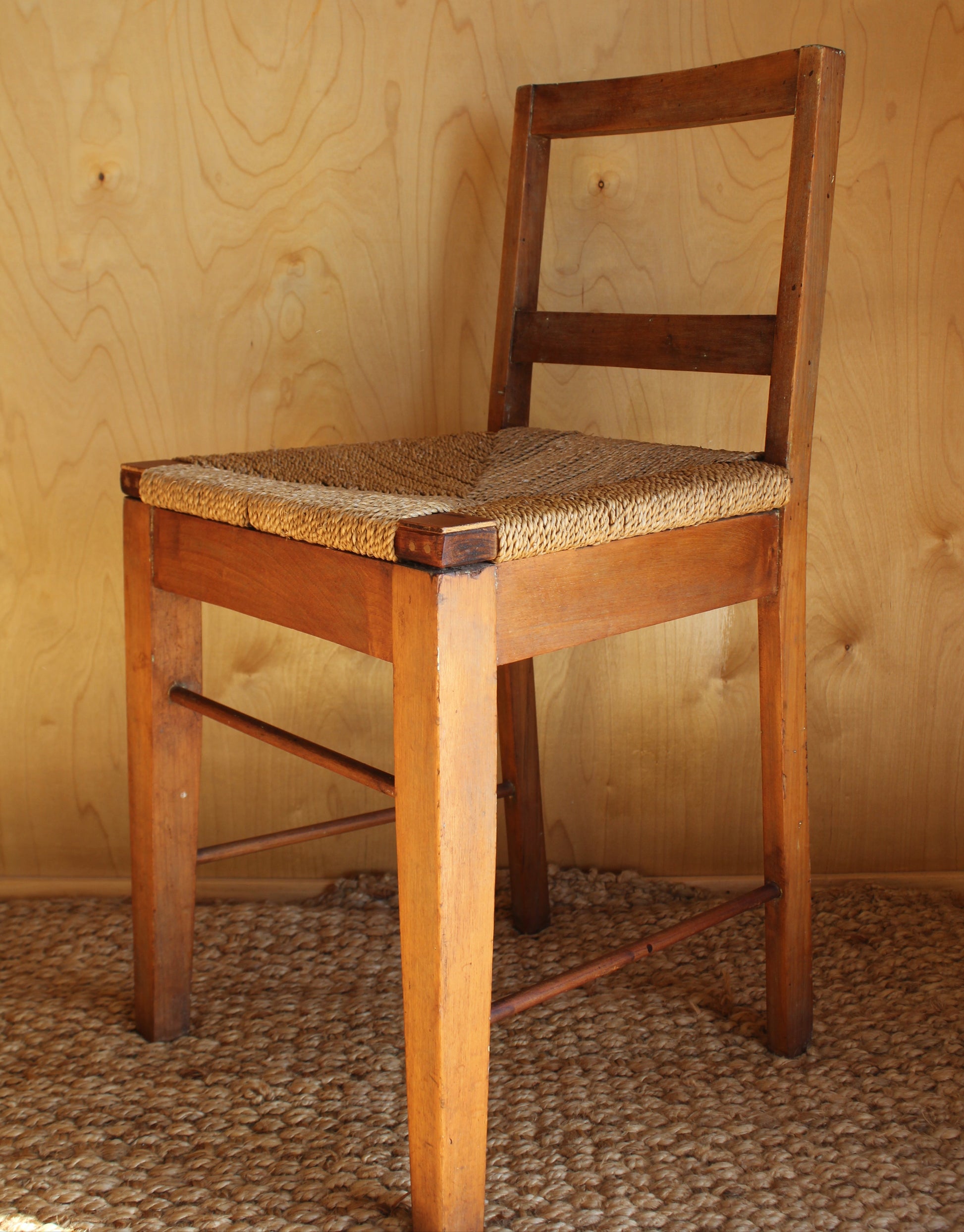 Wooden chair with woven seat against a wooden wall.