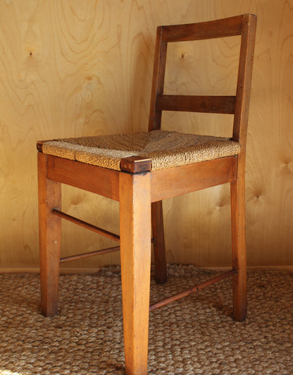 Wooden chair with woven seat against a wooden wall.