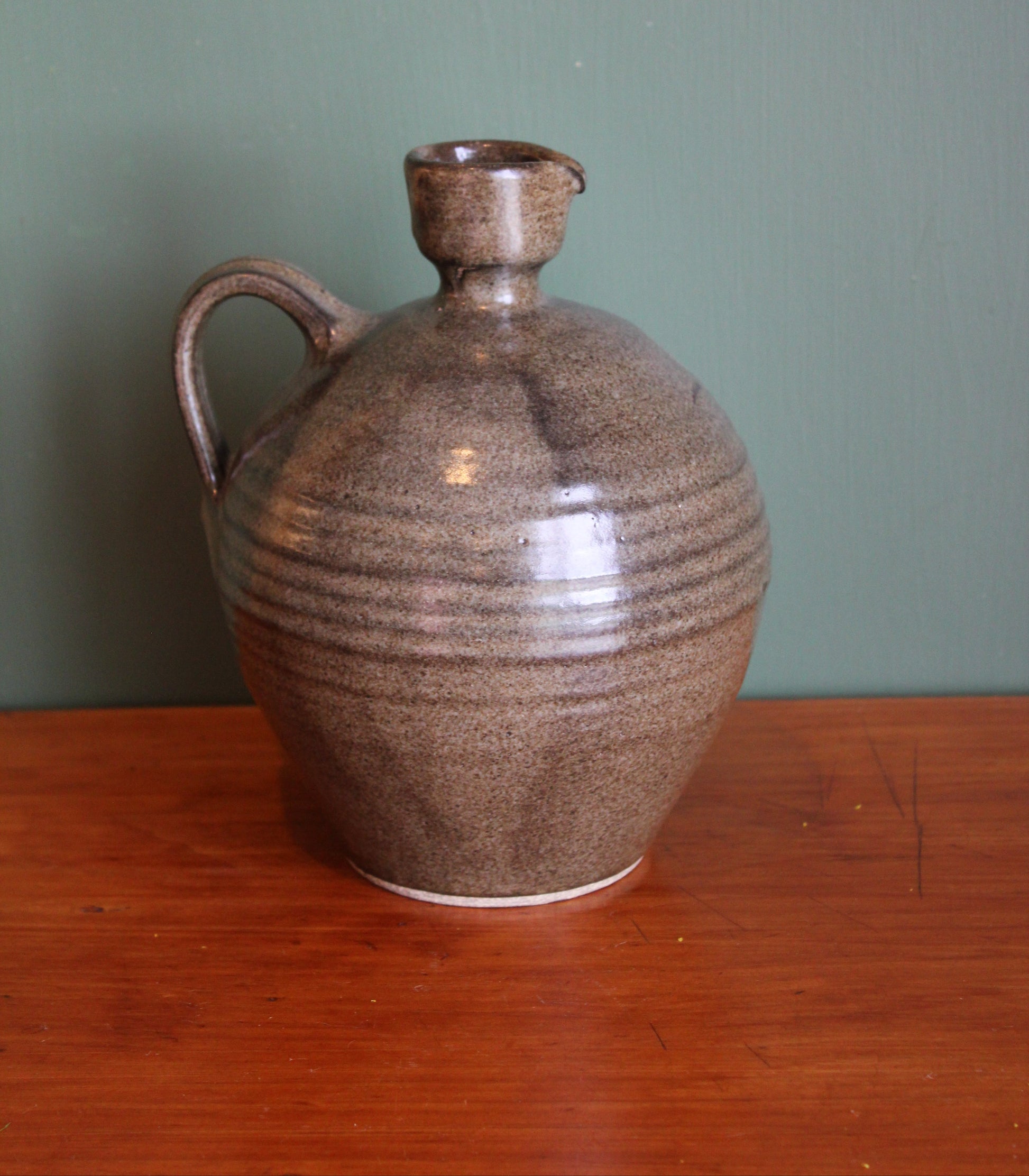 Brown ceramic vase on a wooden surface with a green background