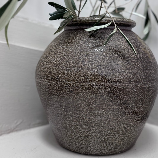 Textured gray vase with greenery on a white surface 