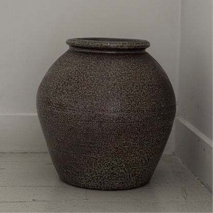 Textured vase on a light wooden floor against a white wall