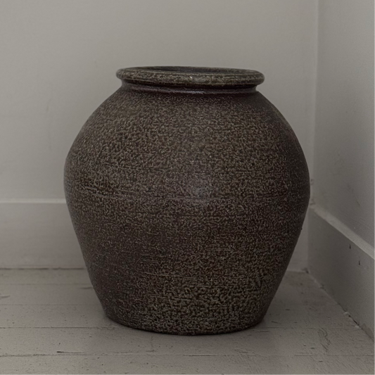 Textured vase on a light wooden floor against a white wall