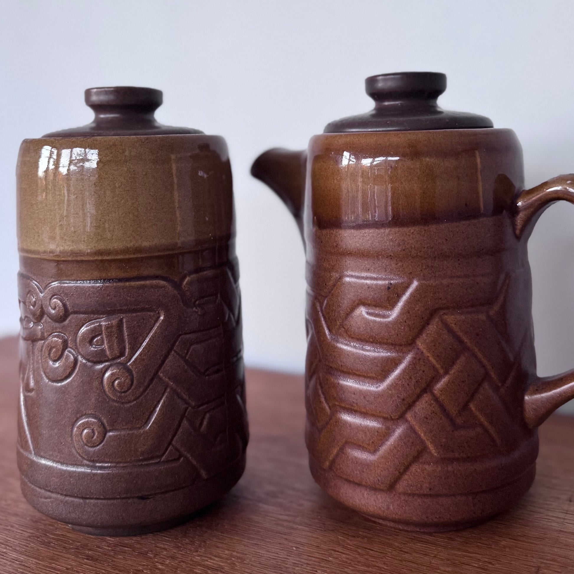 Brown ceramic containers with two designs featuring geometric and swirl carvings on a wooden surface.