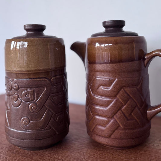 Brown ceramic containers with two designs featuring geometric and swirl carvings on a wooden surface.