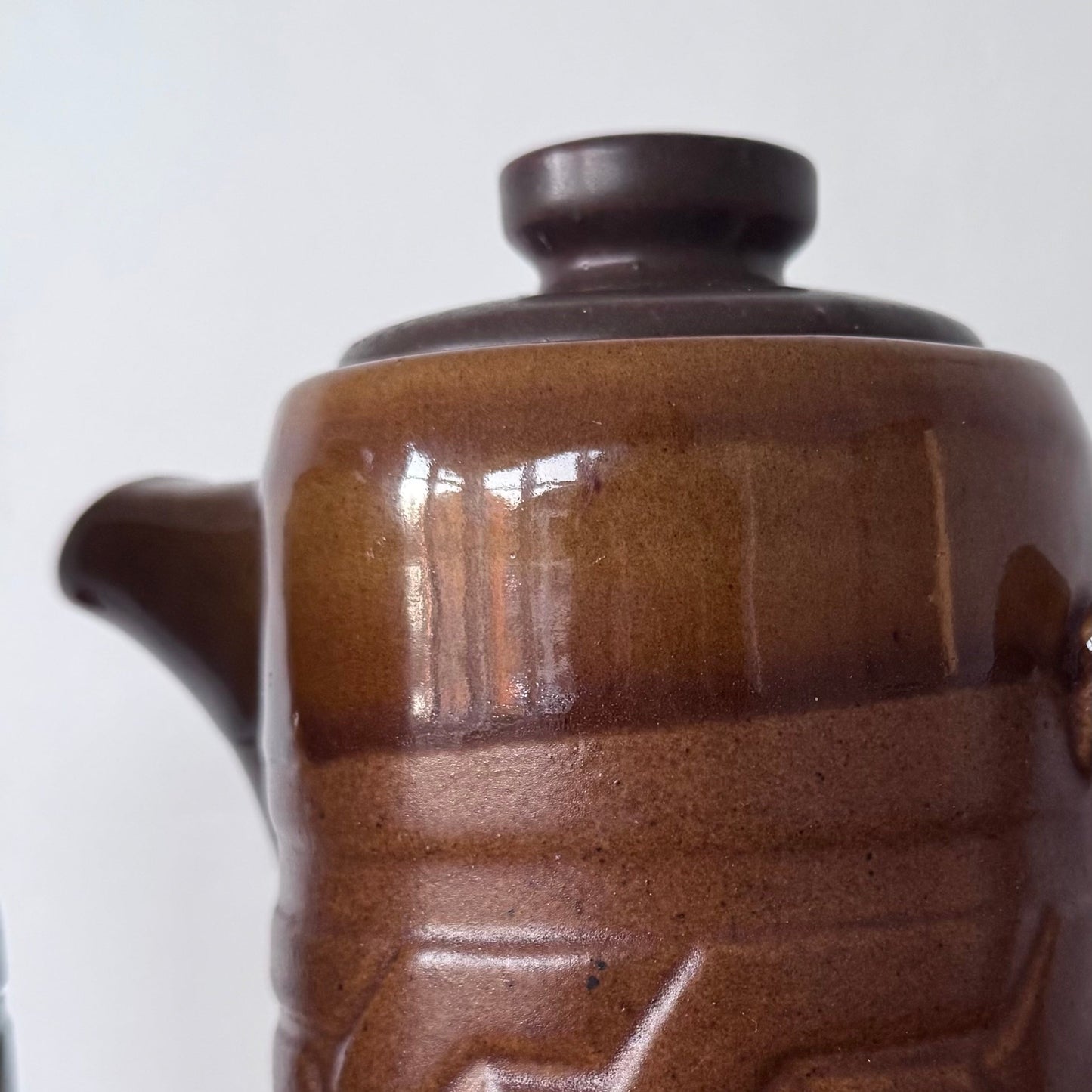 Brown ceramic containers with two designs featuring geometric and swirl carvings on a wooden surface.

