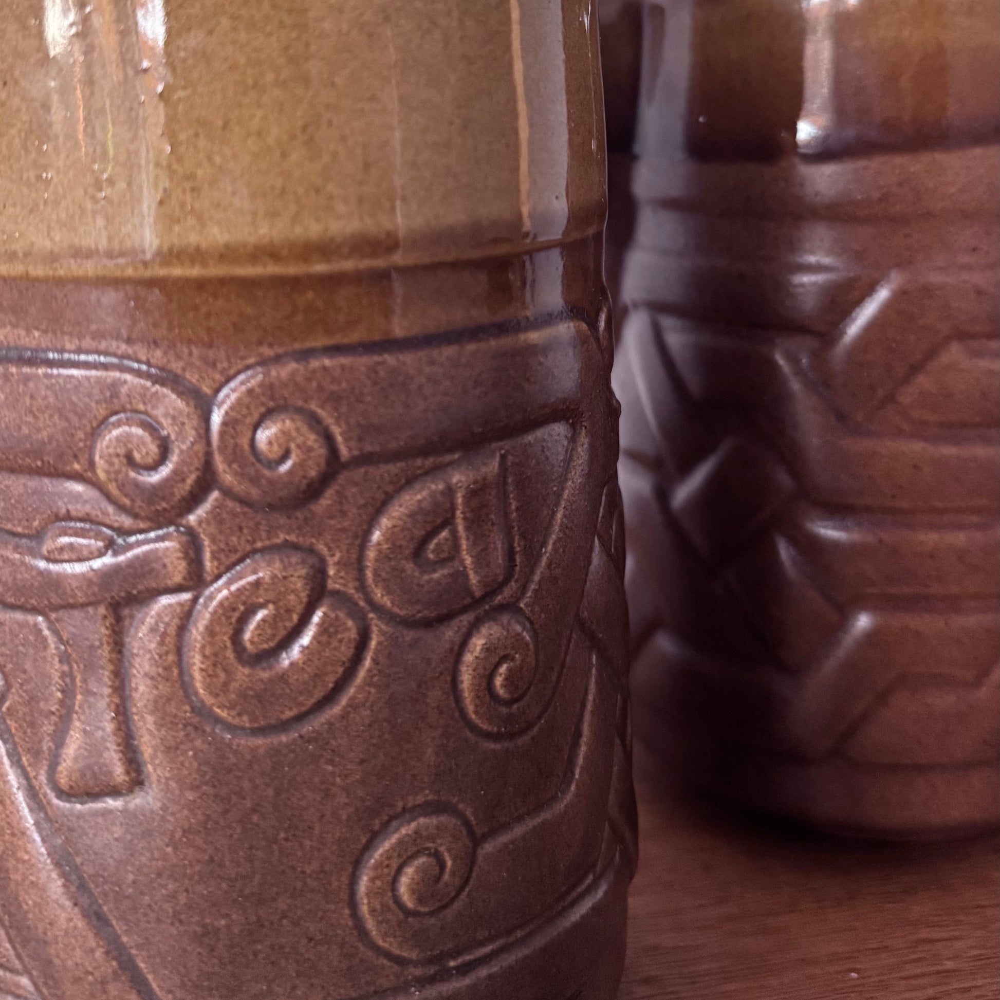 Brown ceramic containers with two designs featuring geometric and swirl carvings on a wooden surface.