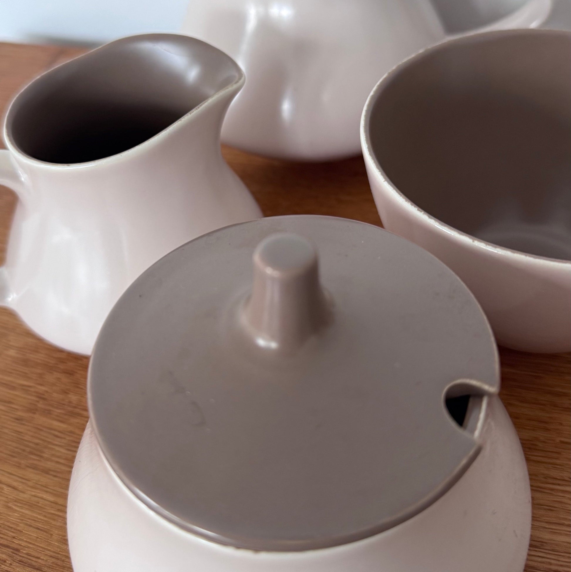 Mauve and brown Poole Pottery cups, jug, and serving dishes stacked neatly on a wooden surface