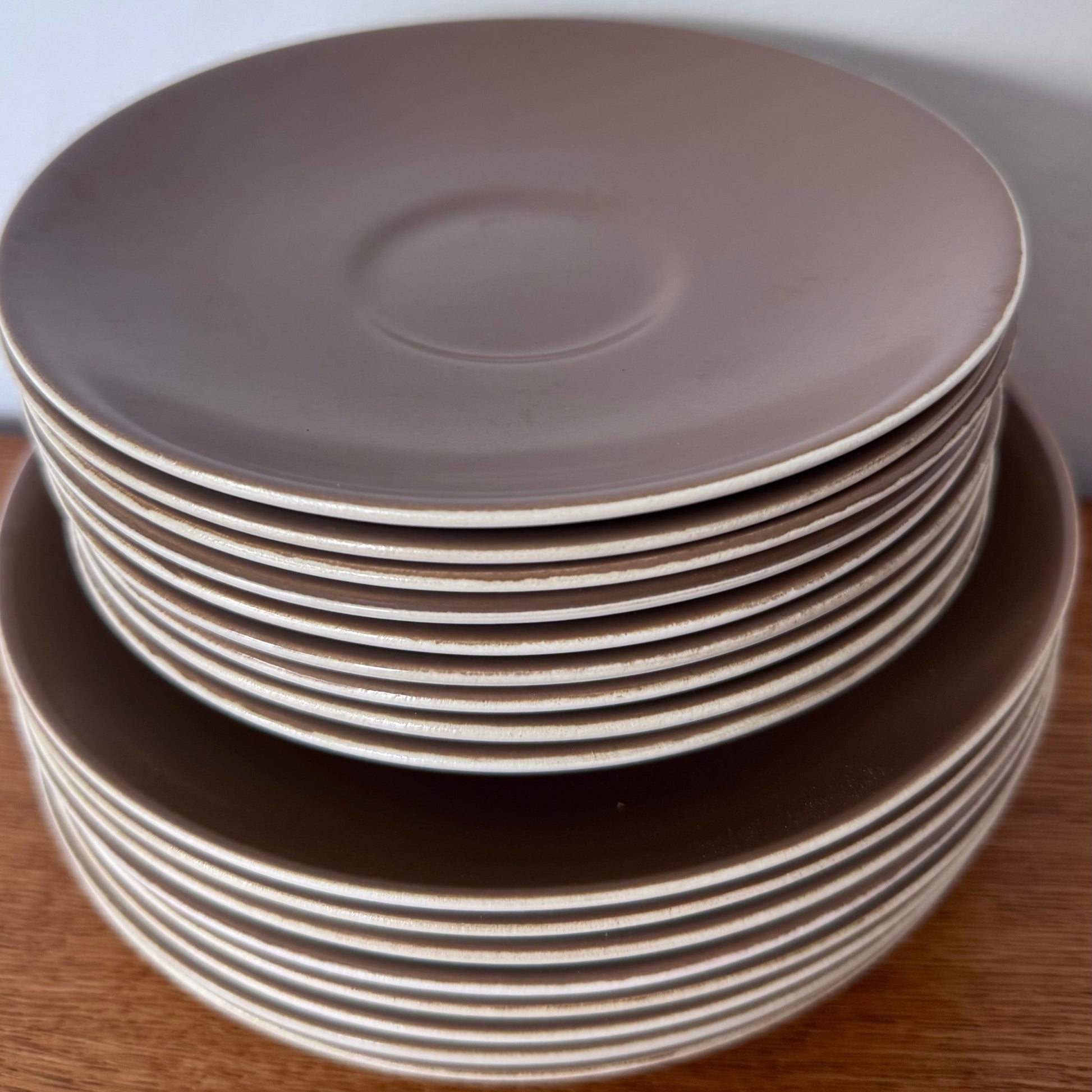 Mauve and brown Poole Pottery cups, jug, and serving dishes stacked neatly on a wooden surface