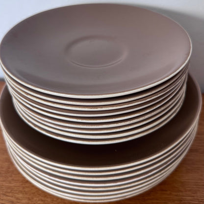 Mauve and brown Poole Pottery cups, jug, and serving dishes stacked neatly on a wooden surface