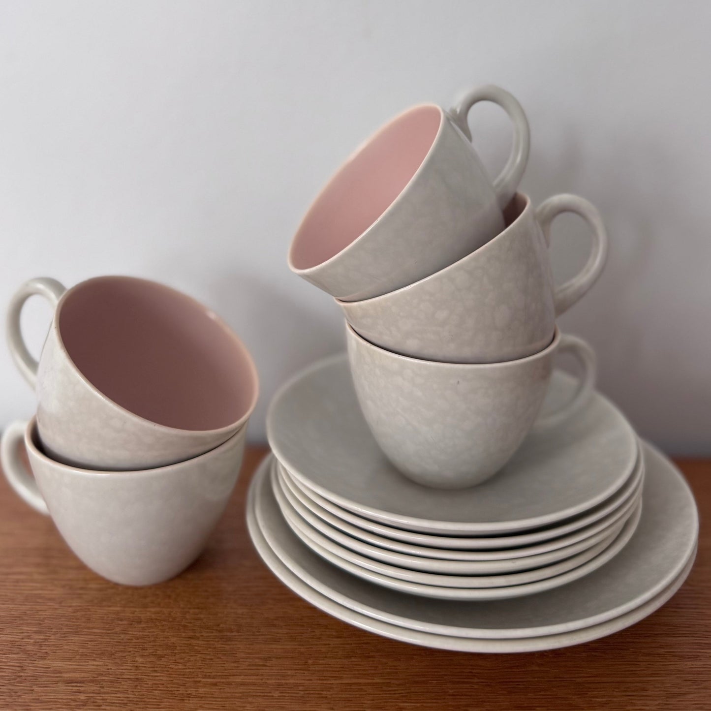 Stack of grey ceramic cups with pink interiors and matching plates on a wooden surface