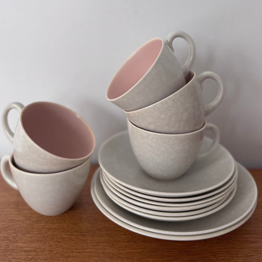 Stack of grey ceramic cups with pink interiors and matching plates on a wooden surface
