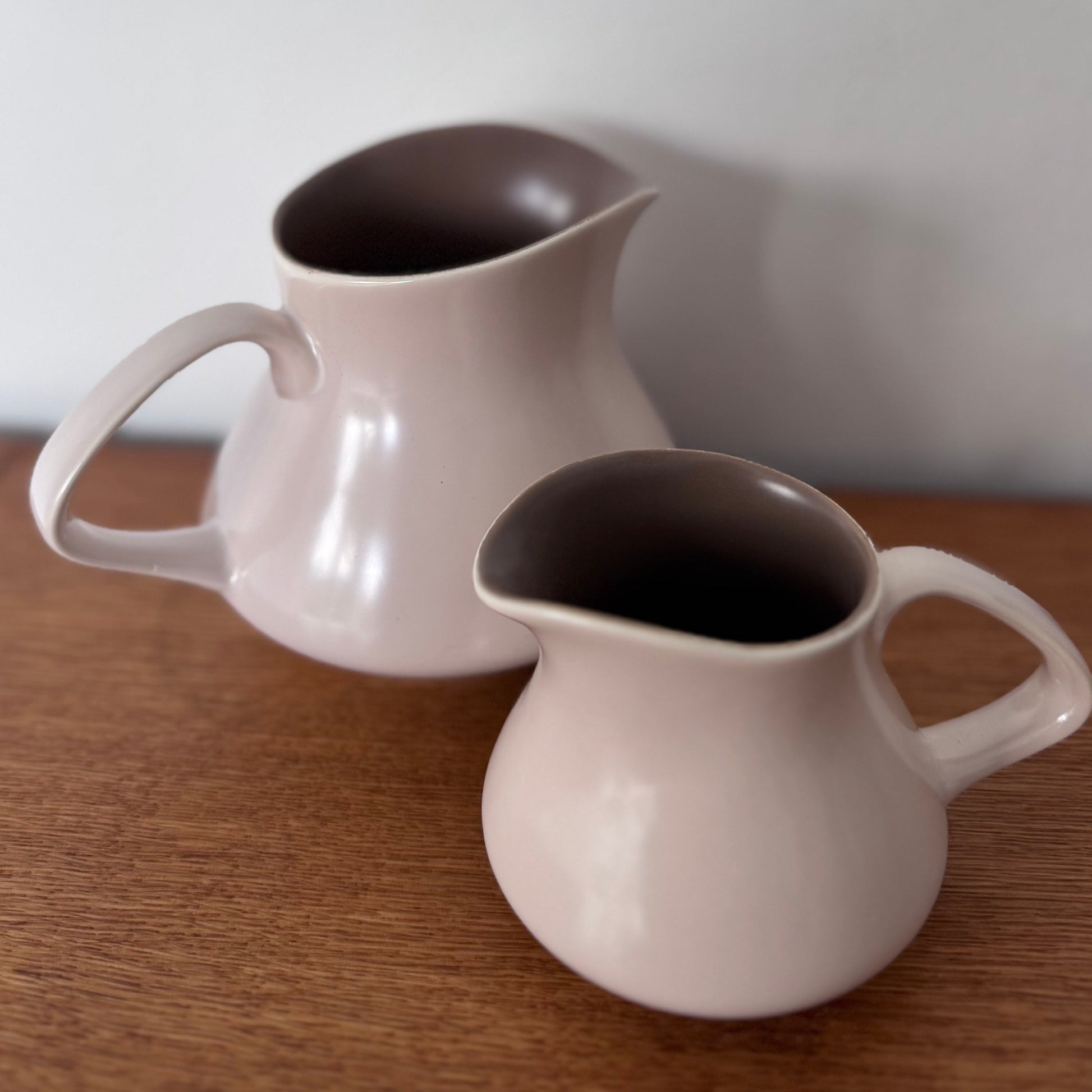 Mauve and brown Poole Pottery cups, jug, and serving dishes stacked neatly on a wooden surface
