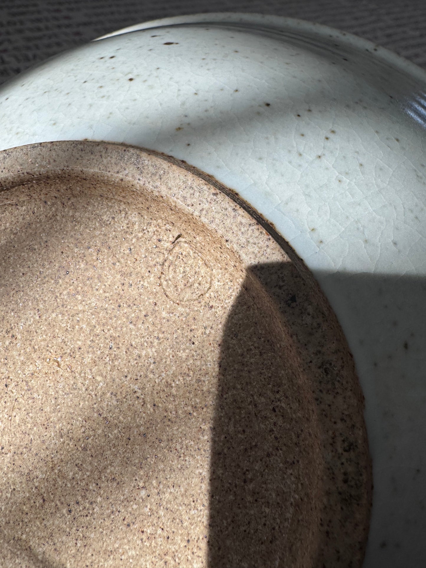Base of a grey ceramic bowl showing a potter’s mark on unglazed clay