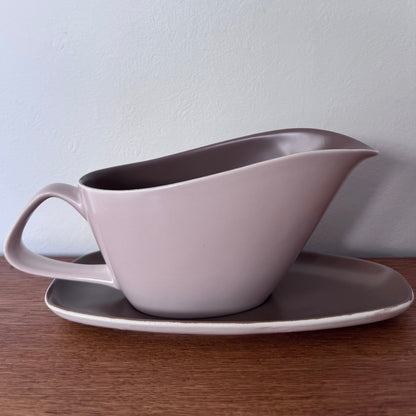 Mauve and brown Poole Pottery bowls and serving dishes stacked neatly on a wooden surface