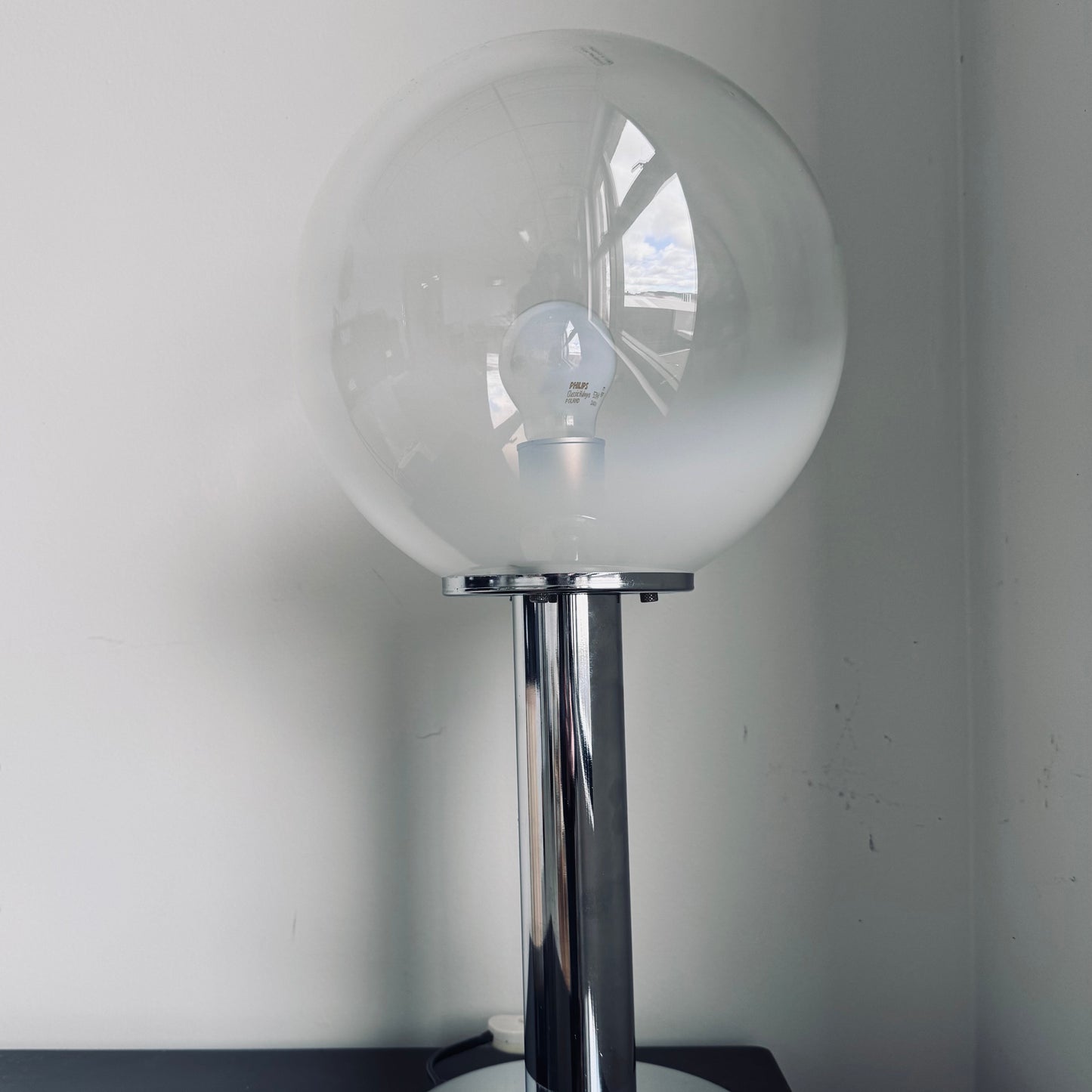 Vintage Targetti Sankey table lamp with a chrome cylindrical base and a frosted glass globe shade, placed on a black surface against a white wall