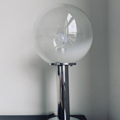 Vintage Targetti Sankey table lamp with a chrome cylindrical base and a frosted glass globe shade, placed on a black surface against a white wall