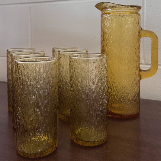 Vintage amber-toned textured glassware set featuring a tall handled pitcher and matching highball glasses with an ice-like pattern