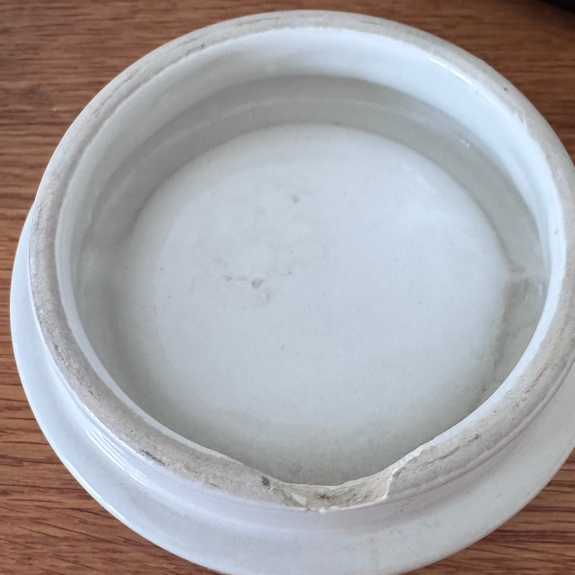 Bottom view of a white ceramic lid showing unglazed edges with visible wear and a chipped section along the rim.