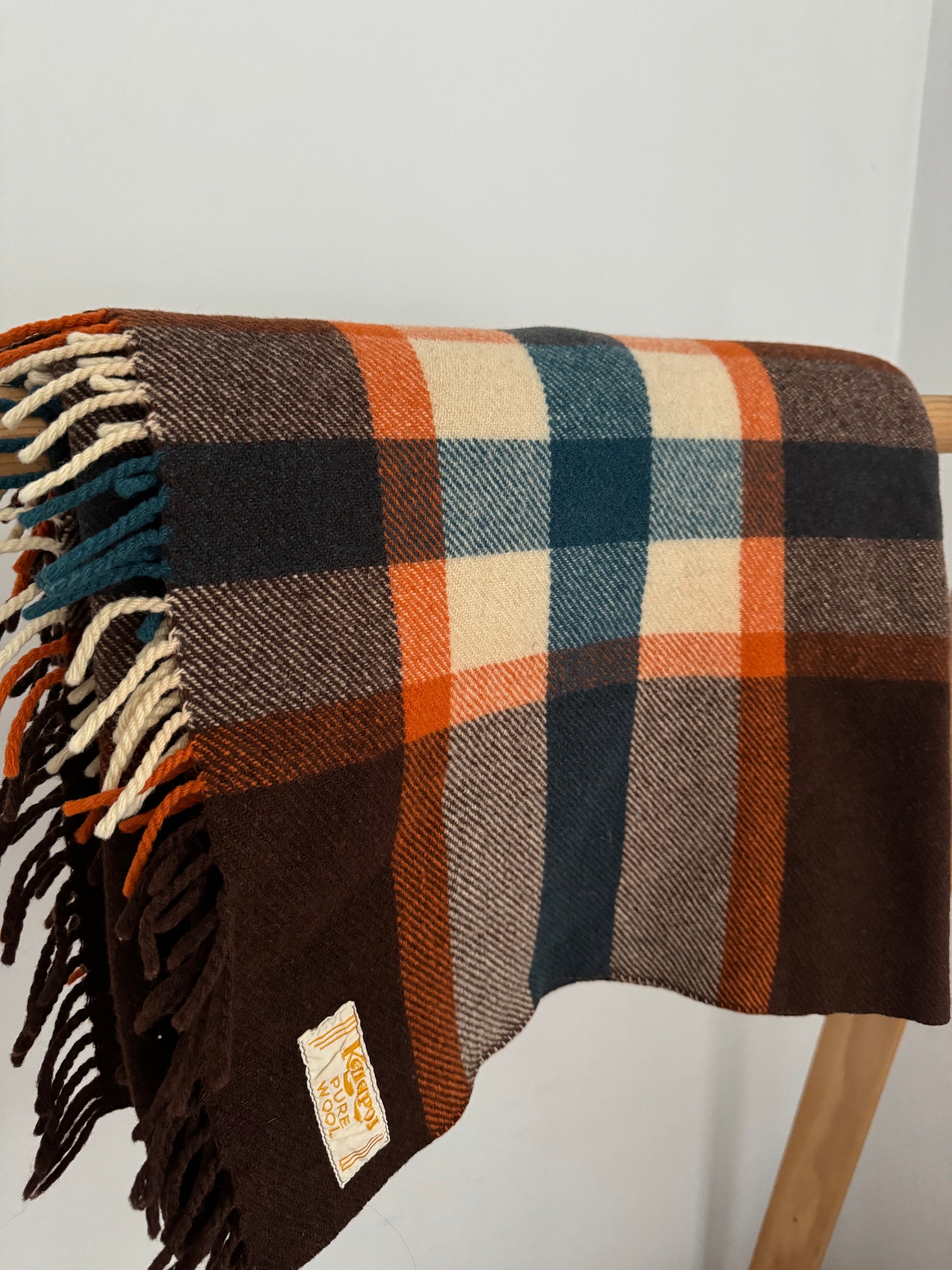 Plaid blanket with fringes draped over a wooden stool on a white background
